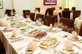 A long table set for a meal with dishes and glasses; several people are seated, in a restaurant.