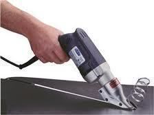 Hand holding a black electric shear cutting through a metal sheet.