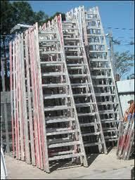 Stack of aluminum ladders leaning against each other outdoors on a sunny day.
