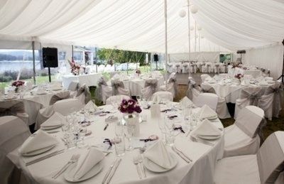 Wedding reception tent with round tables set for guests, with floral centerpieces.