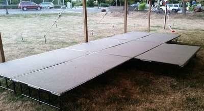 Outdoor stage on grass, gray platforms with metal supports, light-colored wood posts.