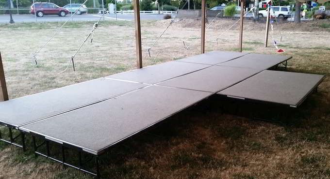 Outdoor stage constructed with gray platforms on grass.