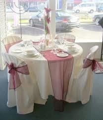 Round table set for a wedding reception, with white tablecloth, burgundy sash, and chair covers.