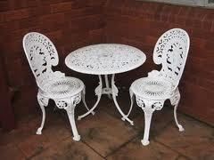 White ornate metal table and two matching chairs on a brick patio.