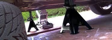 Car on jack stands. Tire on the left. Supports underneath car, driveway setting.