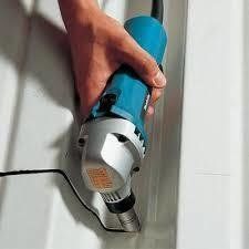 Person using a blue power shear tool to cut a white surface.