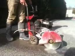 Person operating a red concrete saw, cutting pavement outdoors.