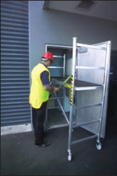 Man in vest and hardhat on scaffolding near building entrance.