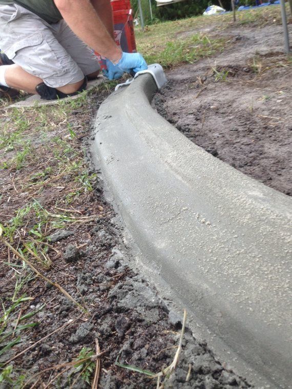 Person smoothing wet concrete curb with a trowel, outdoors.