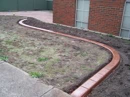 Brown concrete curb edging a grassy area next to a brick building.