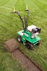 A green sod cutter machine cutting a strip of turf, with a rolled section of sod nearby.