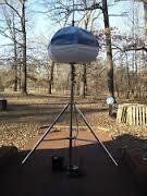 A large, blue and white, round weather balloon on a tripod in a wooded area.