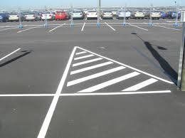 Parking lot with a triangular, striped, white painted area, crossed by white lines.