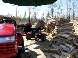 Red tractor and wood splitter under a green umbrella, next to piles of firewood.