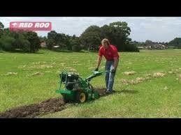 Man using a green trencher on a grassy field, creating a trench.