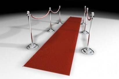 Red carpet with silver stanchions and rope barriers, on a white surface, symbolizing a VIP entrance.