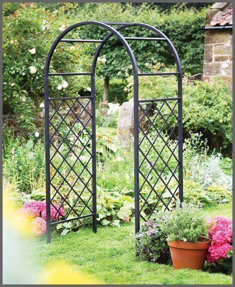 Black metal garden arbor in a lush green garden with potted plants.