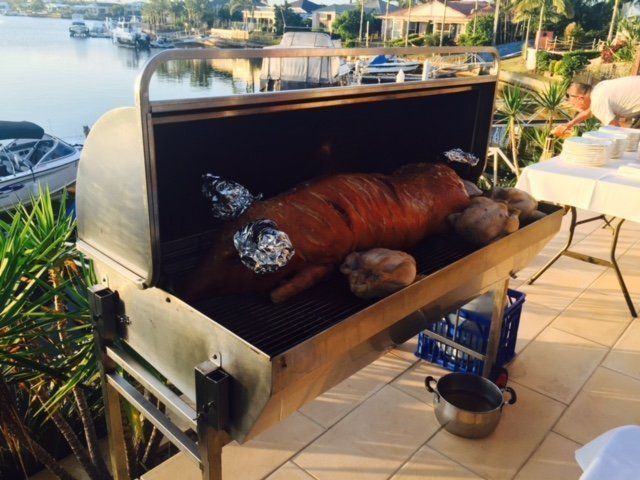 A whole roasted pig on a large outdoor grill, ready for a party next to a waterway.