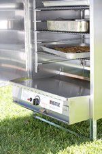 Stainless steel smoker with trays inside, sitting on grass.