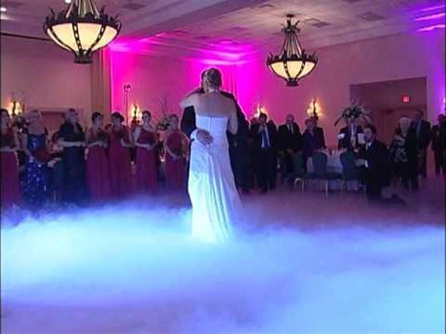 Bride and groom dance on a fog-filled dance floor, surrounded by guests at a wedding reception.