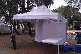 White pop-up tent with walls, table inside, outdoors near trees and a truck.