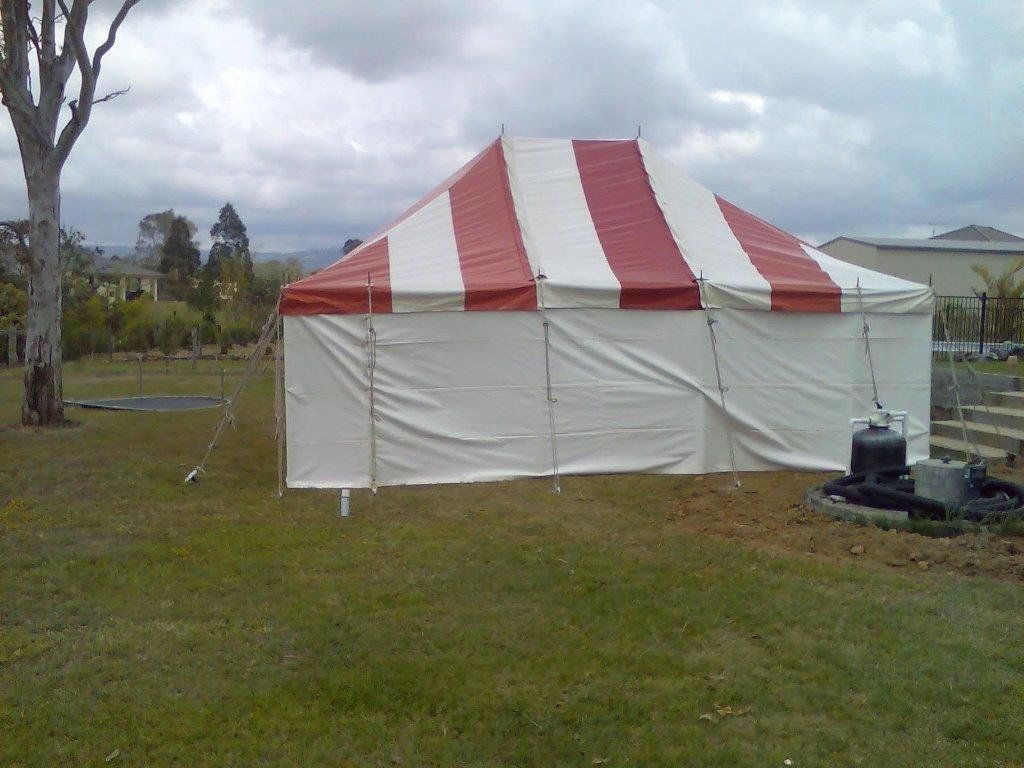 Red and white striped tent set up on a grassy lawn, cloudy sky.