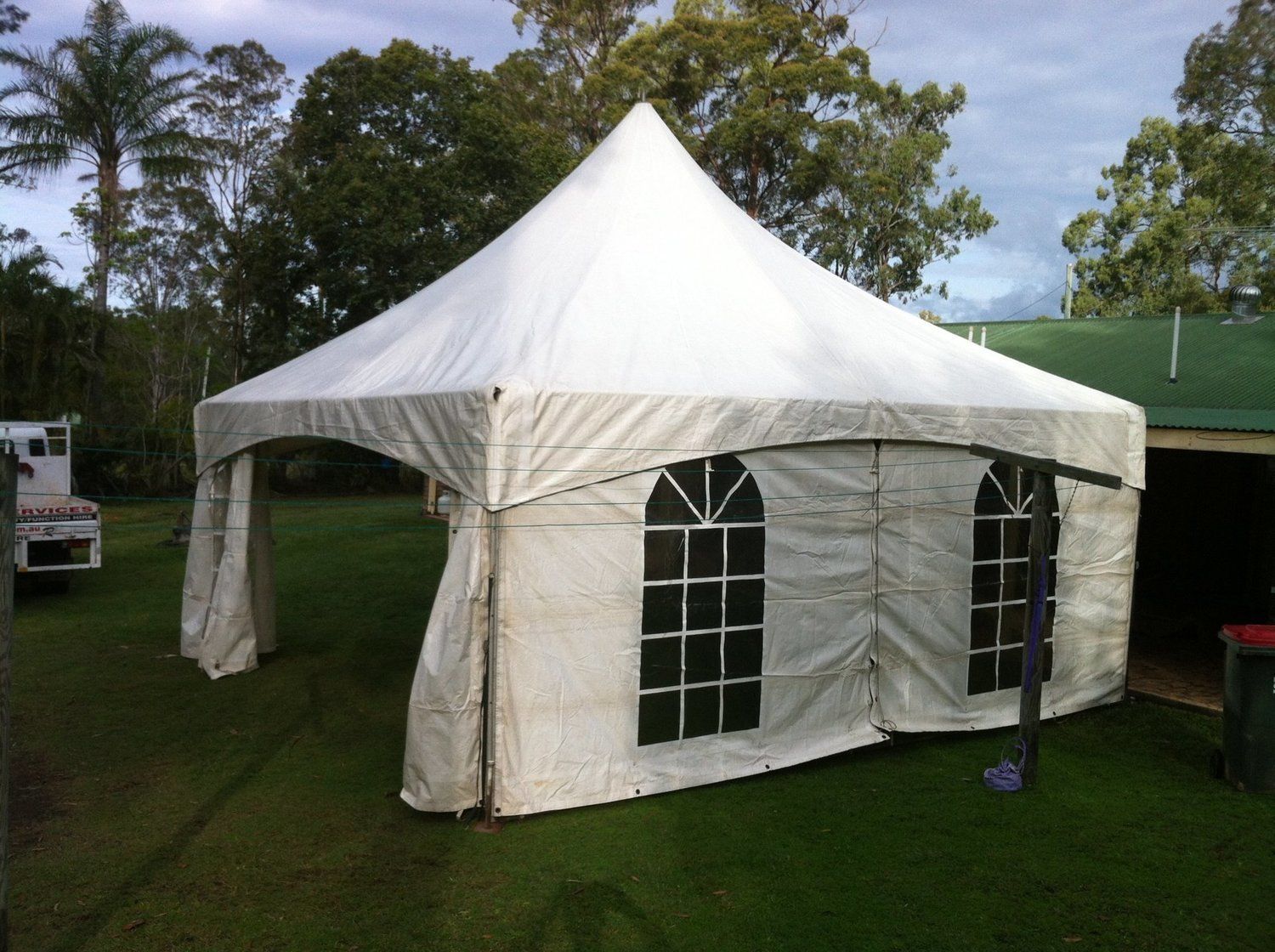 White tent with arched windows set up on green grass with trees in the background.