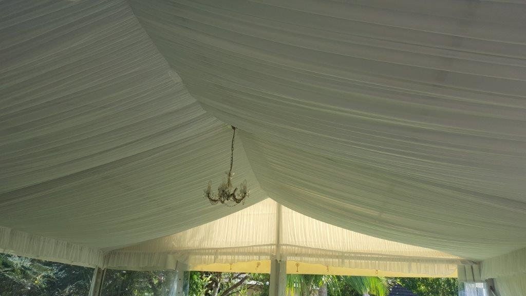 White tent interior with draped ceiling, a chandelier, and a view of the outside.