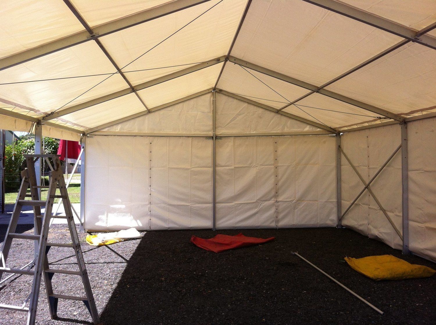Inside view of an empty white tent with a ladder, set outdoors on a gravel surface.