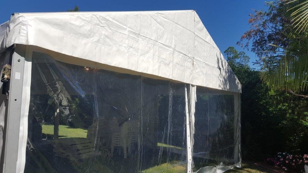 White tent with clear sides set up outdoors on a sunny day.