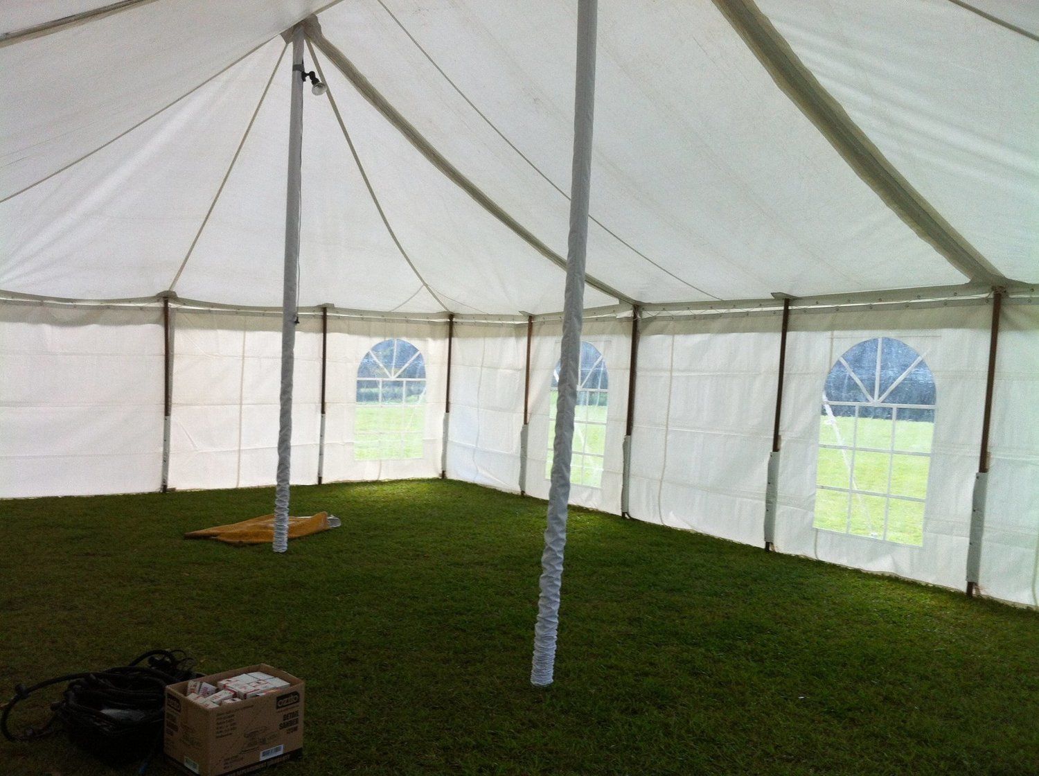 Inside of a white tent with grass flooring, featuring multiple arched windows and central support poles.