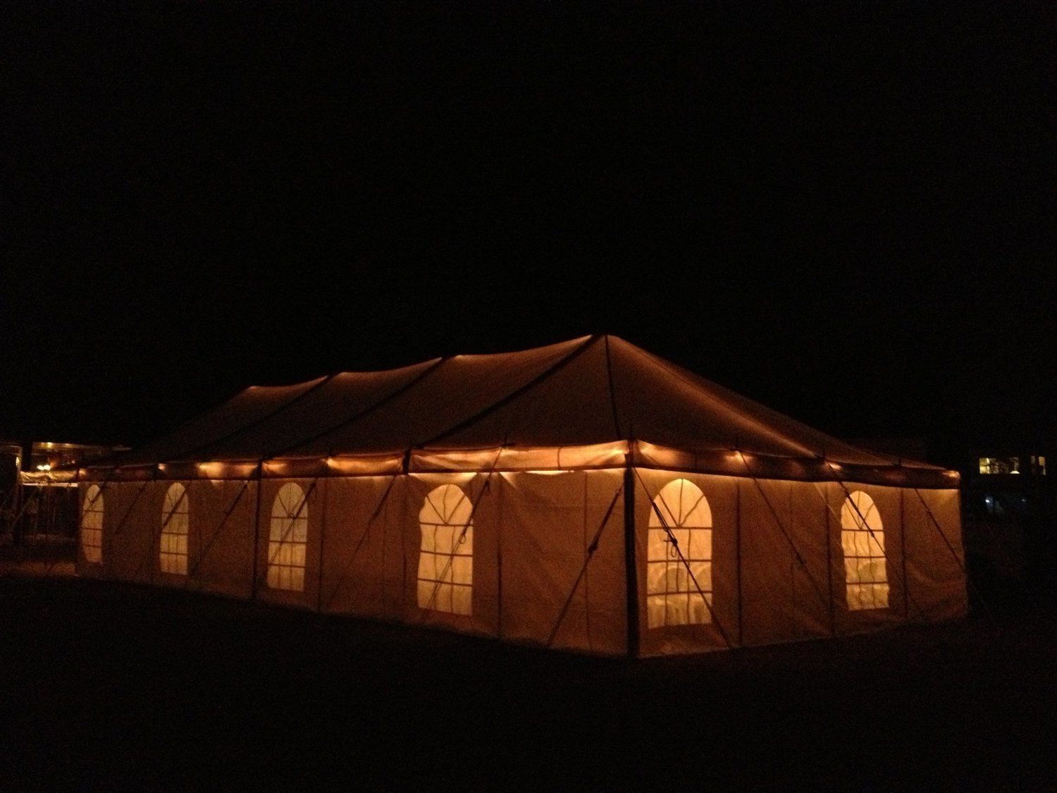 Large illuminated tent at night. Beige tent with arched windows, lit from within, against a dark sky.