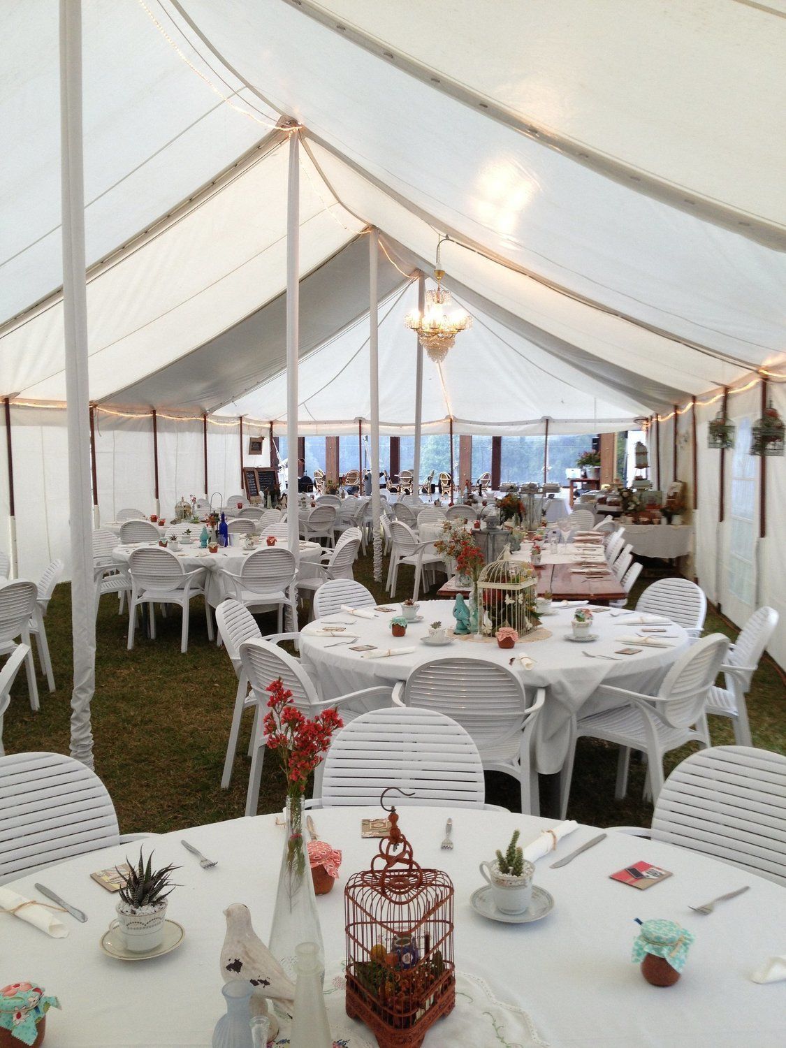 White tent interior with round tables set for a gathering, white chairs, and floral centerpieces.