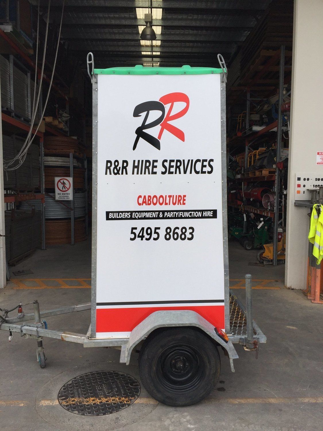 Trailer with R&R Hire Services signage: white, red, black logo, phone number. In front of a warehouse.