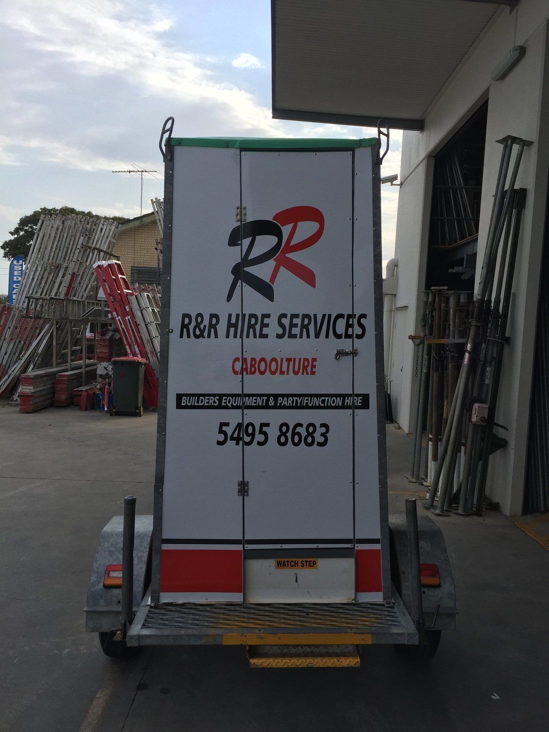 Rear view of a trailer with R&R Hire Services logo, parked outside a warehouse.