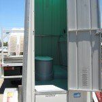 A portable toilet with the door open, showing the inside; a light green glow illuminates the interior.