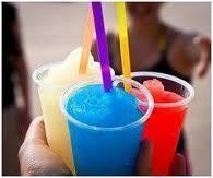 Hand holding four colorful slushies with straws.
