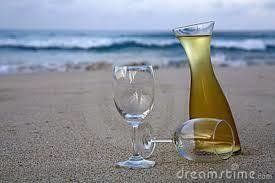 Wine bottle and glasses on a sandy beach with ocean waves in the background.
