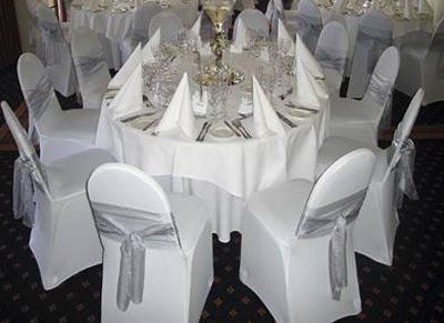 Round table set for a formal event, featuring white tablecloth, chairs with silver bows, and elegant place settings.