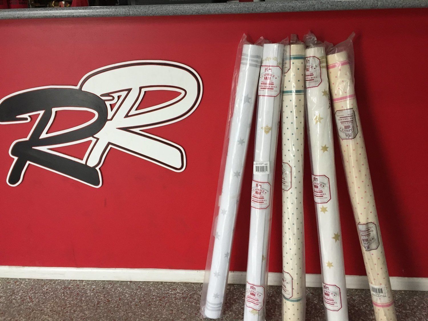 Rolls of wrapping paper next to a red wall with a white and black logo.
