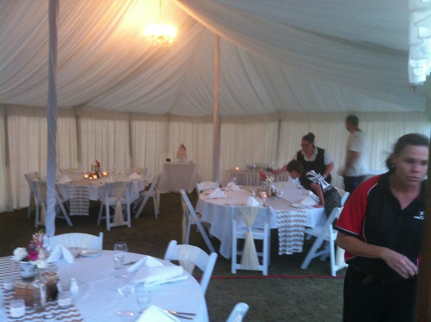 Inside a white tent, set tables and people setting up for an event.