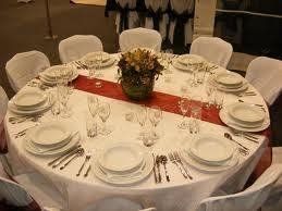 Round table set for a formal dinner with white plates, chairs, and centerpiece.