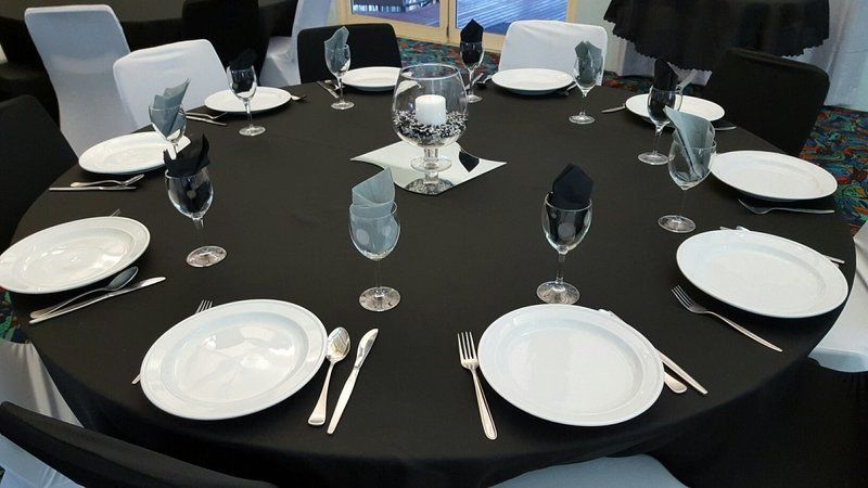 Round table set for a formal dinner with black tablecloth, white plates, silverware, and center candle display.
