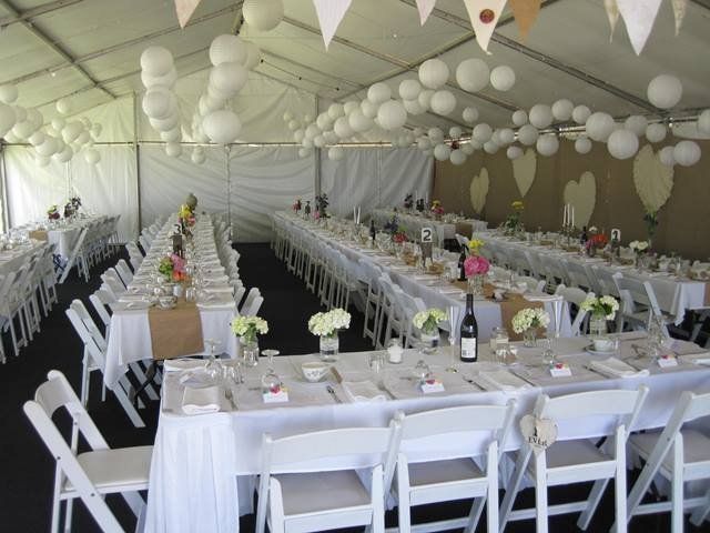 Wedding reception in a white tent with long tables set for guests, decorated with flowers and paper lanterns.