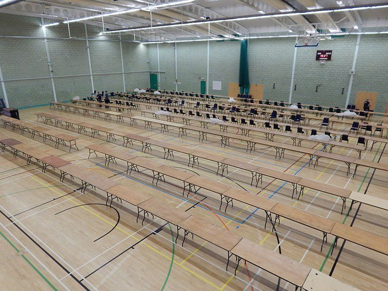 Long rows of tables and chairs set up in a gymnasium; likely for an exam or testing.
