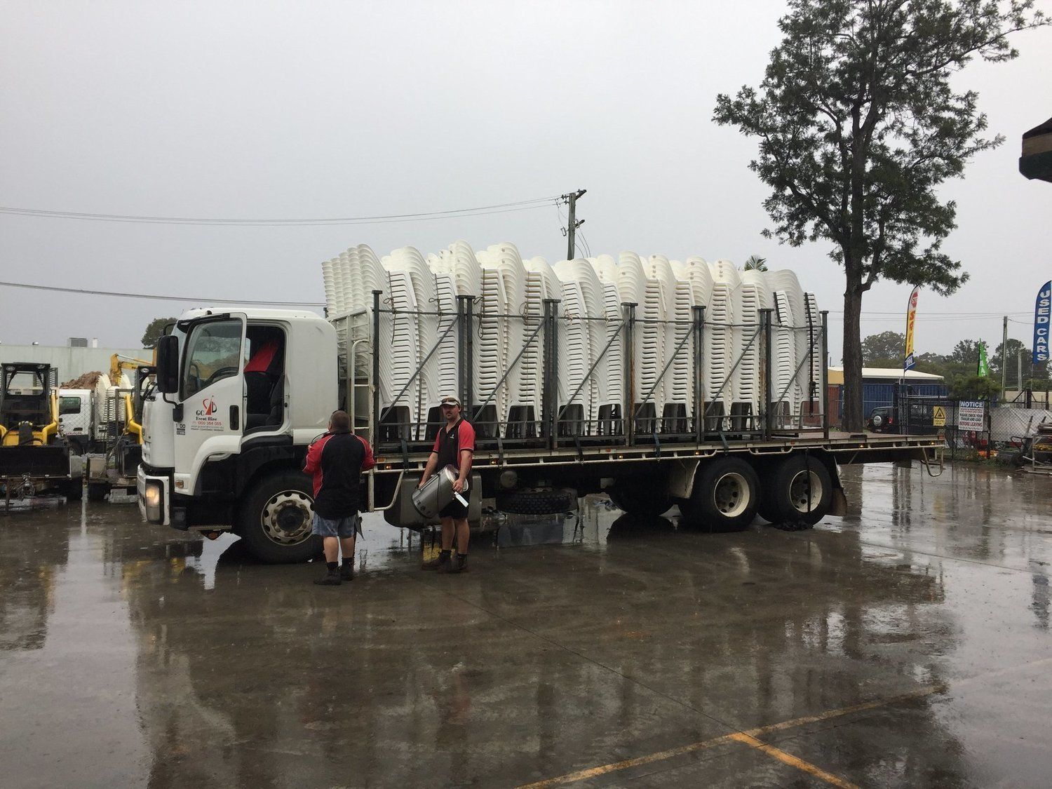 Truck loaded with white folding chairs being unloaded by two people in the rain.