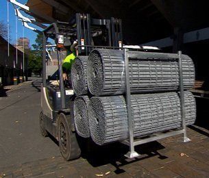 Forklift carrying rolled metal mesh rolls in a warehouse.