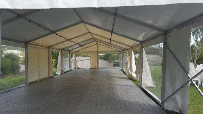 Inside view of a large, white event tent with clear sidewalls and a wood-like floor, set outdoors.