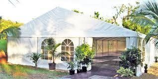 White tent with arched windows, open doorway, and potted plants set on green grass.