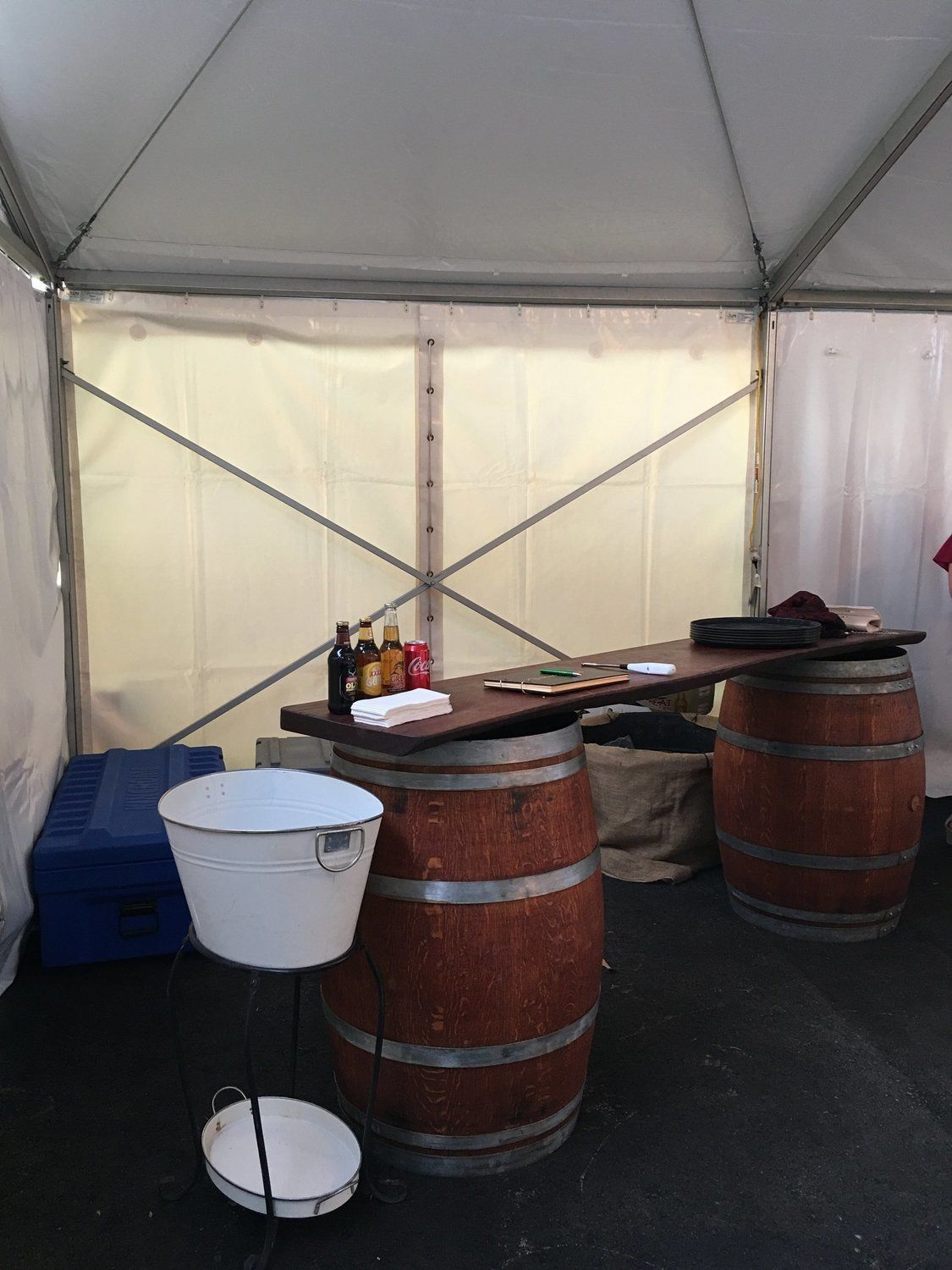 Wine tasting setup inside a tent, featuring wooden barrels, a counter with bottles, and a metal bucket.